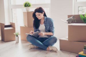 Woman sitting on the floor, surrounded by boxes, writing in a notebook, waiting for Philly movers